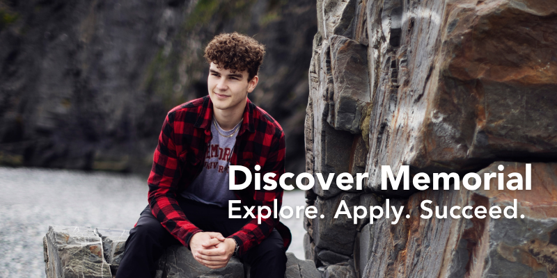 A student wearing a red and black plaid shirt and a Memorial University t-shirt sits on rocky cliffs near the coast, looking off to the side with a relaxed expression. The text on the image reads 'Discover Memorial. Explore. Apply. Succeed.'